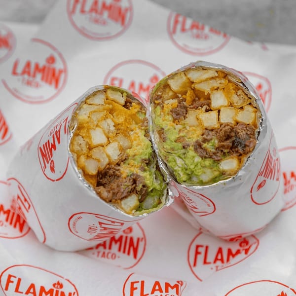 A large El Flamin Taco burrito, cut in half, revealing carne asada, guacamole, and fries.