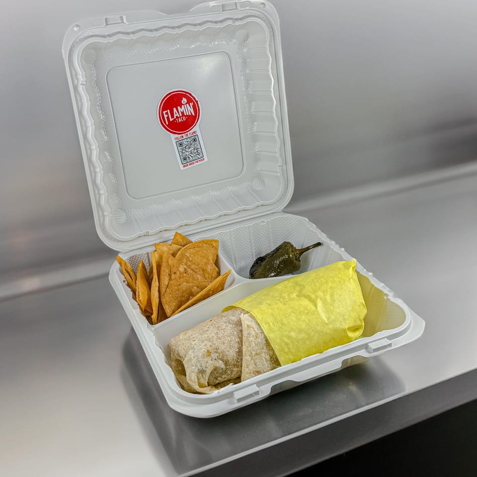 El Flamin Taco burrito in a takeout container with tortilla chips and a roasted pepper.