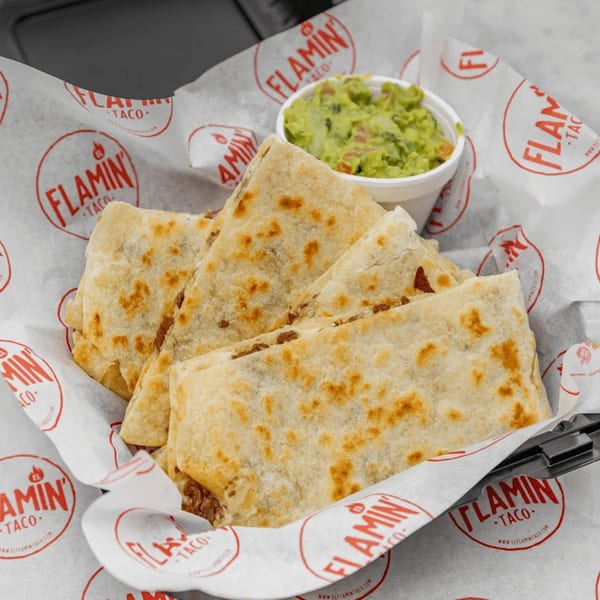 El Flamin Taco quesadillas, cut into triangles, served with a side of guacamole in branded paper.