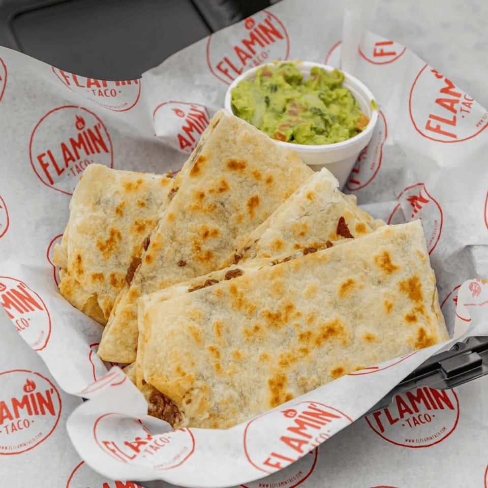 El Flamin Taco quesadillas, cut into triangles, served with a side of guacamole in branded paper.