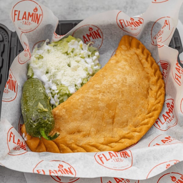 A large, golden-fried empanada with a side of shredded lettuce, cheese, and a green pepper.