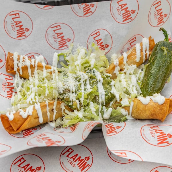 El Flamin Taco taquitos with lettuce, cheese, sour cream, guacamole, and a large green pepper.