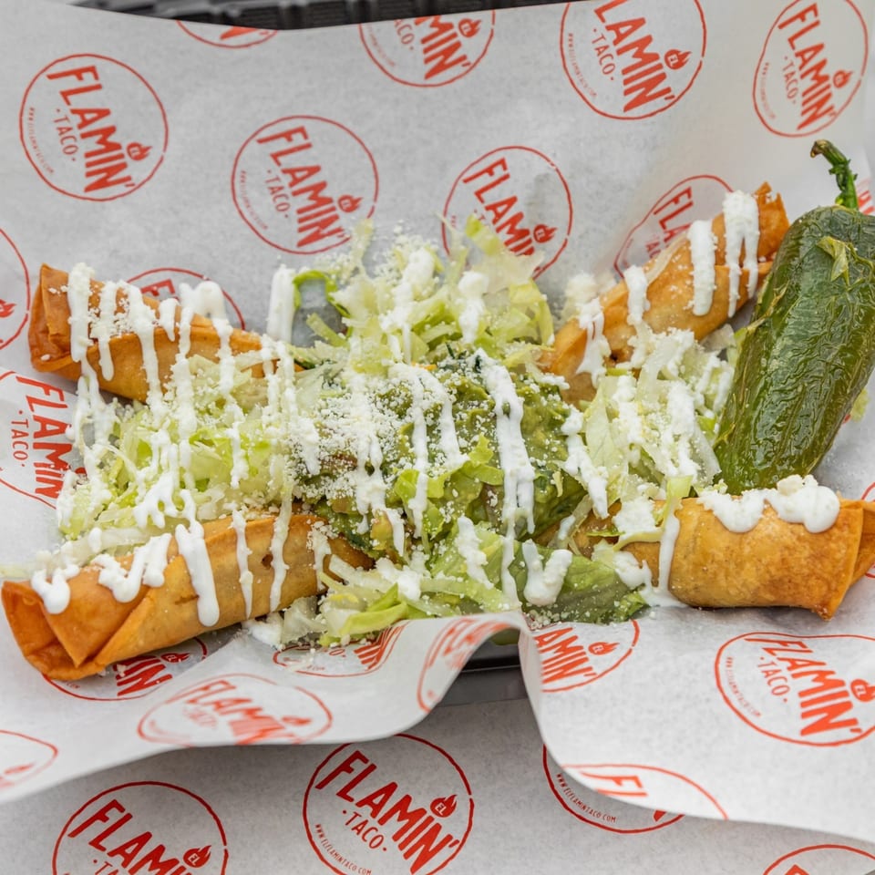 El Flamin Taco taquitos with lettuce, cheese, sour cream, guacamole, and a large green pepper.